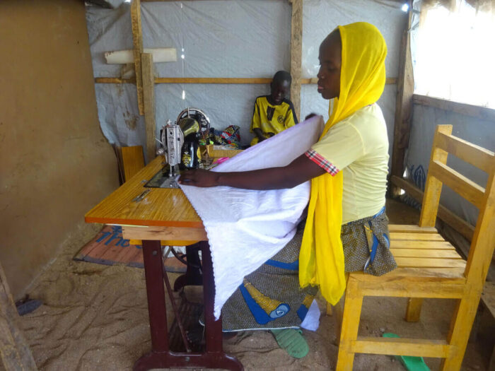 A woman using a sewing machine in a shelter