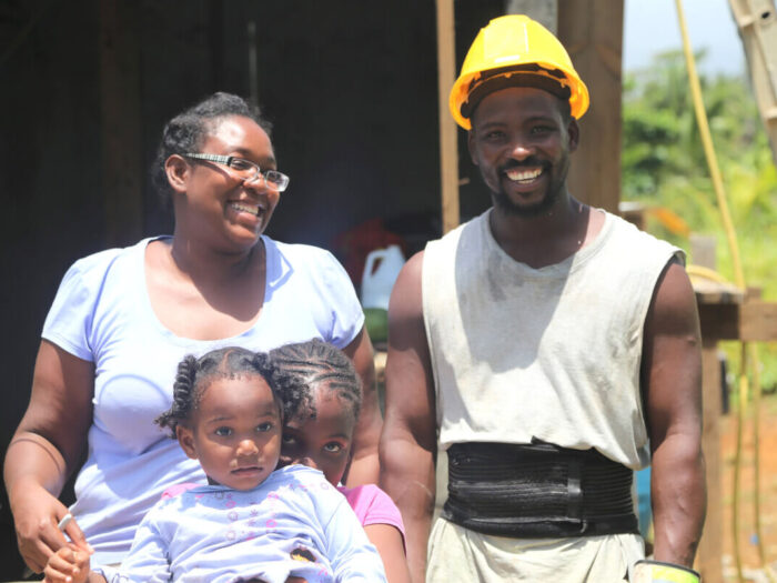 A smiling family helping to fix shelter after hurricanes Irma and Maria in Dominica