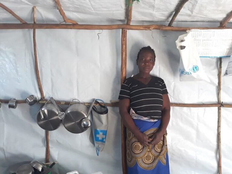 Woman from Malawi stands in emergency shelter with aid items after Cyclone Idai