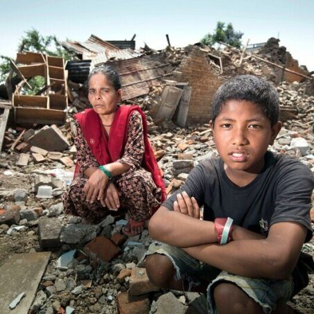 A lady and young boy sitting on rubble and debris in Nepal