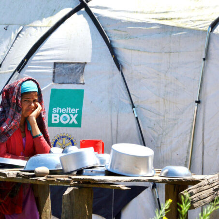 Lady sitting at a table of pots and pans in front of her Shelterbox tent