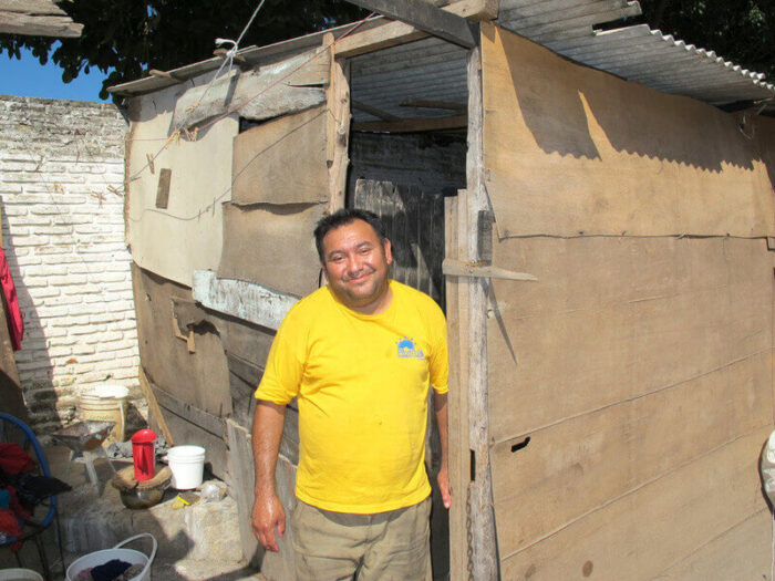 A smiling man standing at the threshold of his hand built home