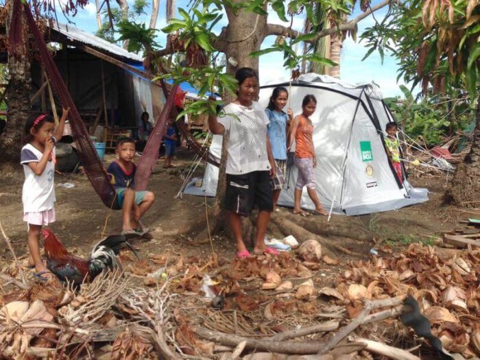 Family in the Philippines stand under trees by ShelterBox tent after Typhoon Haiyan