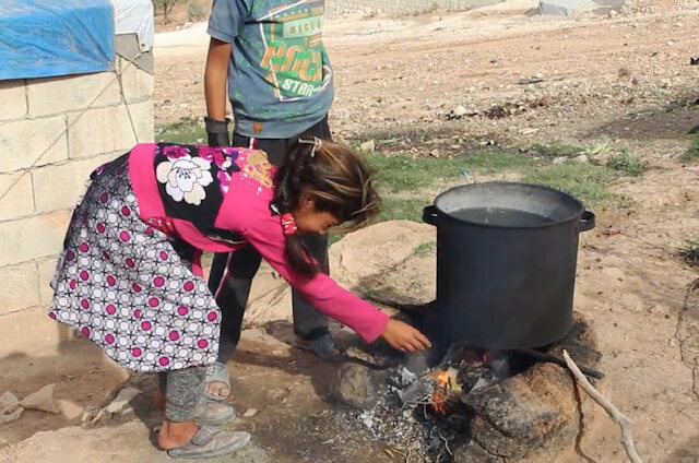 Young girl cooks over fire in displacement camp in Syria