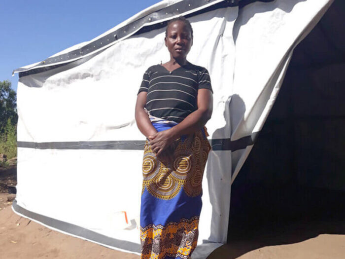 Woman from Malawi stands in front of emergency shelter after Cyclone Idai