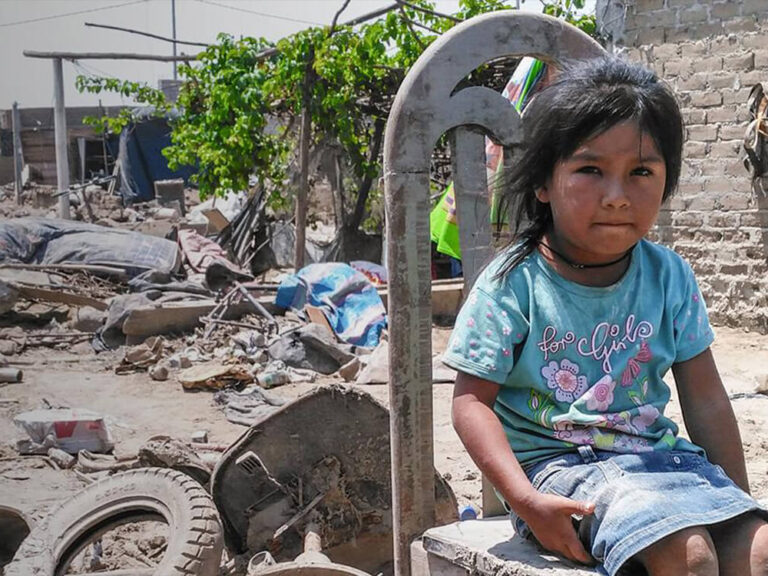 Child sitting on chair between rubble - Flooding in Peru banner