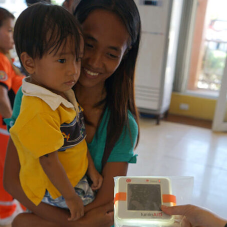 Woman carrying child looking at luminAid - Philippines