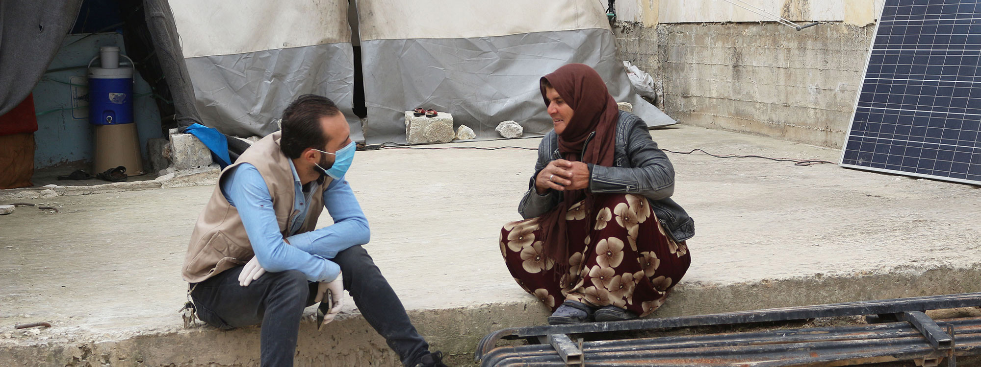 Man in face mask talking to a woman in a Syrian refugee camp during the coronavirus pandemic