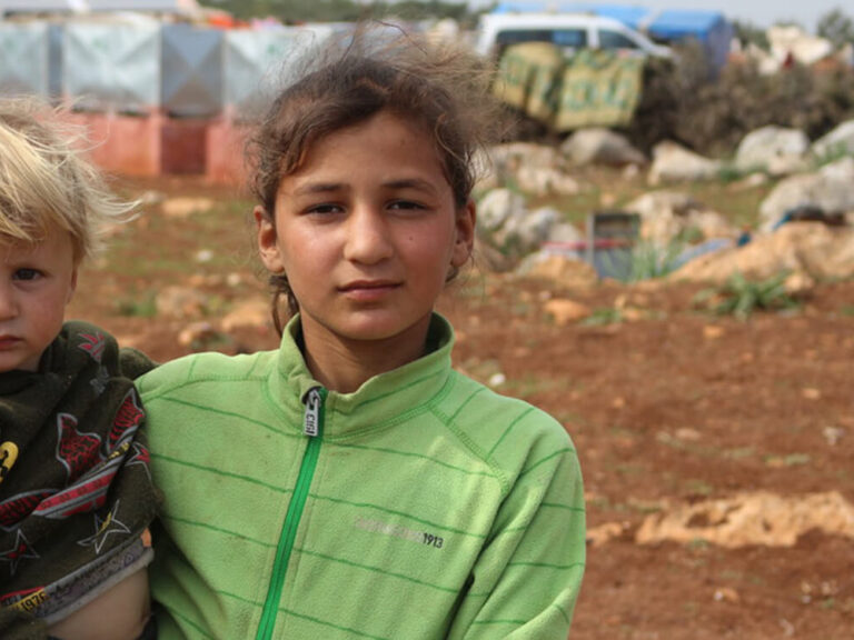 A girl hold a small child in a Syria camp