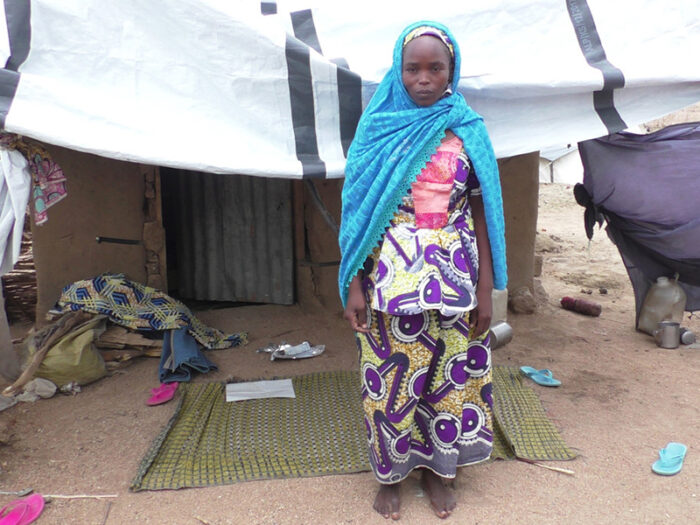 Woman in bright blue scarf standing outside her shelter in Cameroon