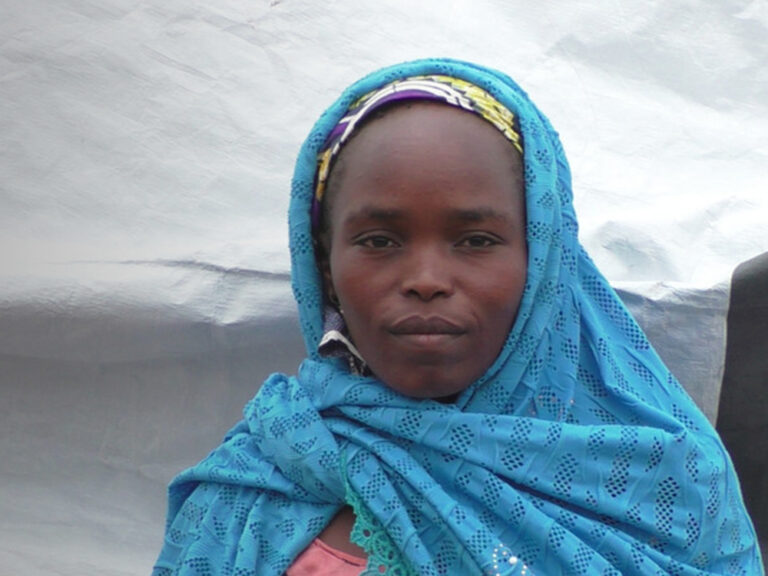 woman in a blue scarf standing in front of her shelter