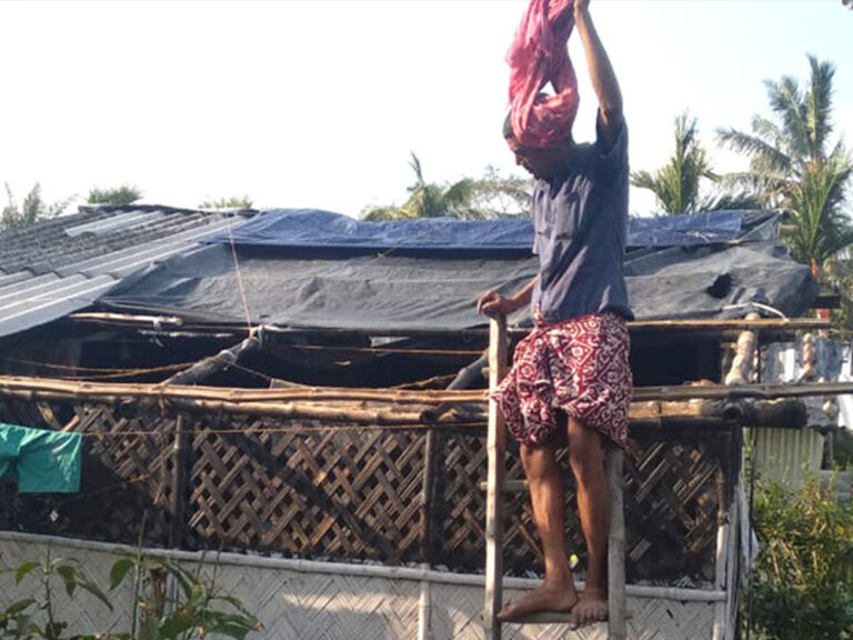 A man up on a ladder assessing the damage on his shelter in India after Cyclone Amphan