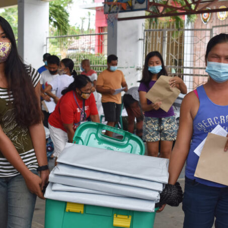 women in facemasks carry shelterbox aid in philippines