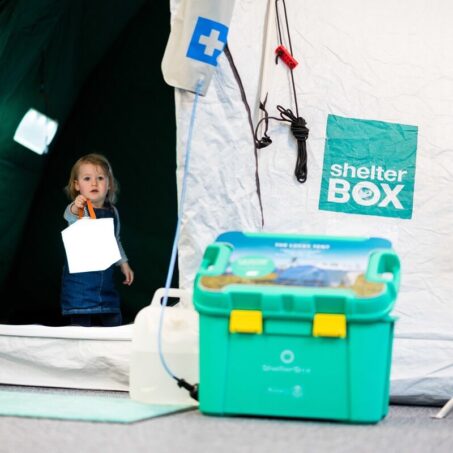 Child holding a solar light in the entrance of a tent, next to a green box in the ShelterBox visitor centre