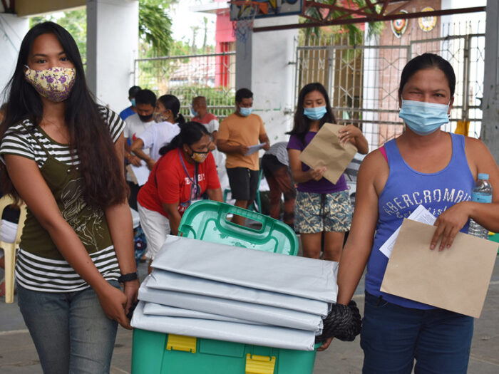 2 women in medical masks carrying a small shelter box in the Philippines