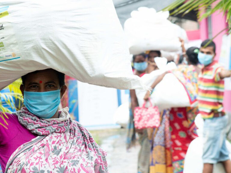 Woman wearing a medical mask and carrying ShelterBox aid on her head