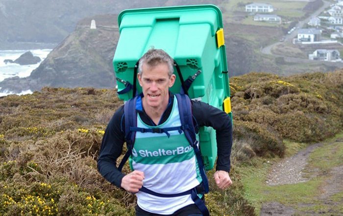 Man running along box carrying green ShelterBox on his back