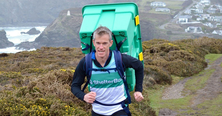 Man running along box carrying green ShelterBox on his back