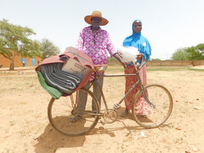 A man and a girl standing behind a bicycle holding aid.