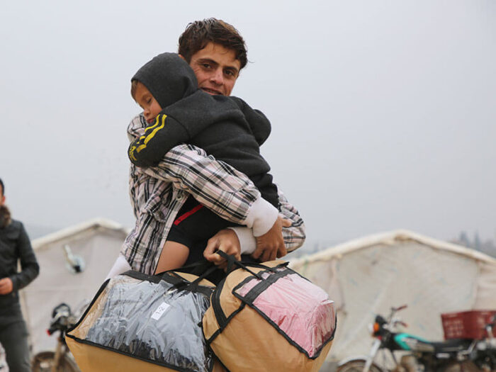 father carries child and bags in syria
