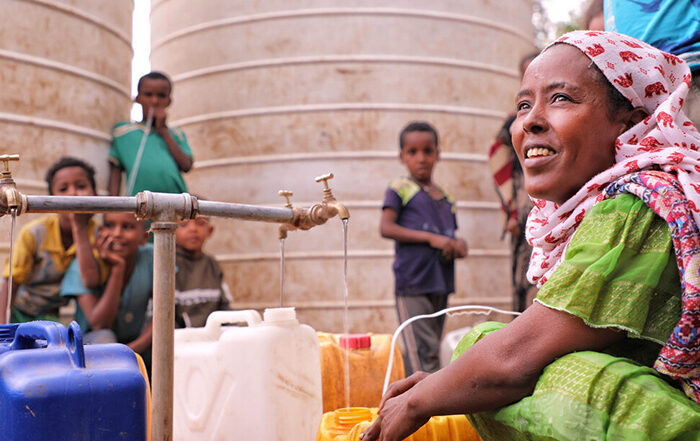 Woman and children next to water tap filling plastic bottles in Tigray, Ethiopia