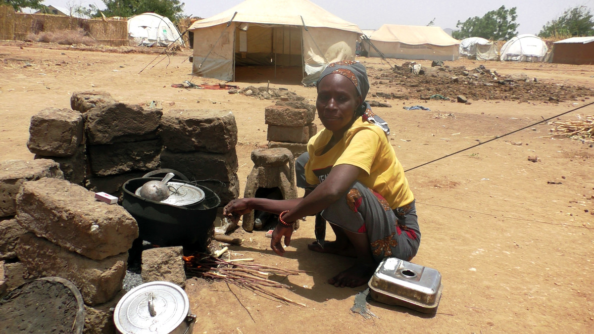 Woman crouching down with a kitchen set outside tent in Cameroon