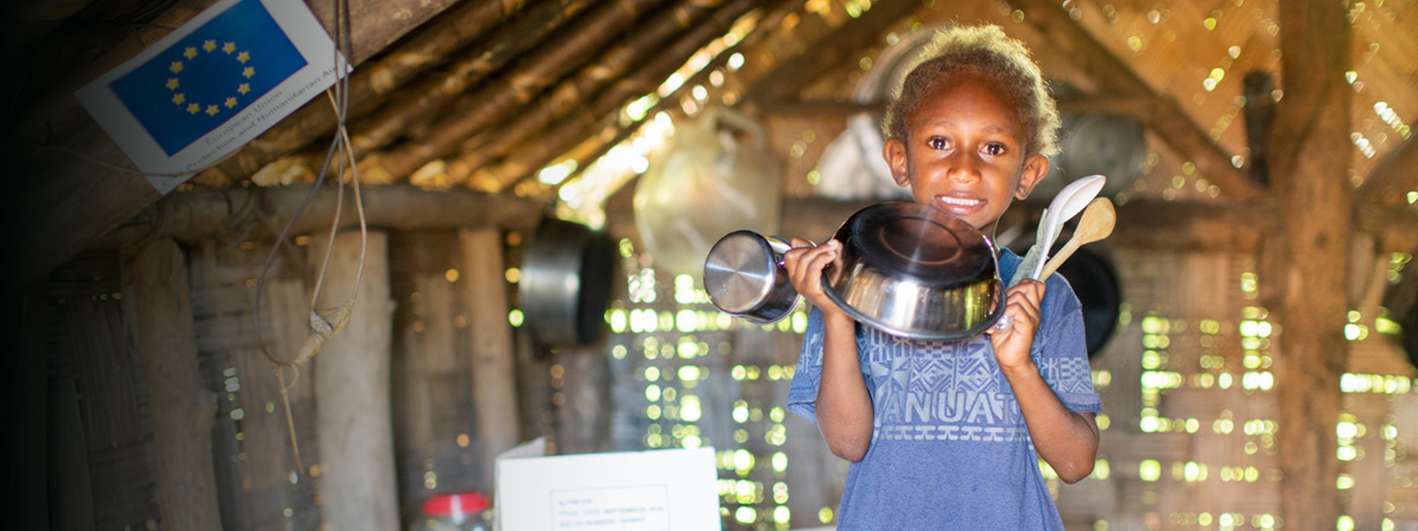 child holding a kitchen set and smiling inside a shelter on Vanuatu