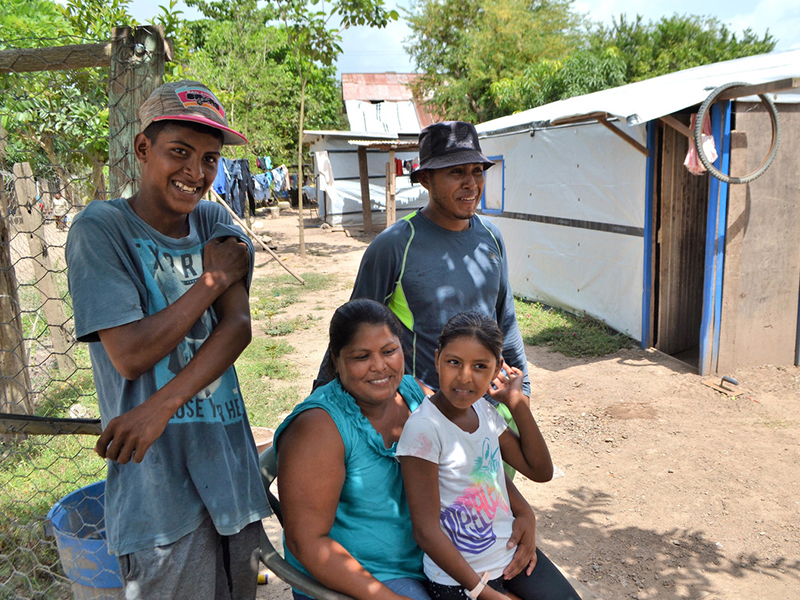 A woman sitting down with her three children next to shelters in Honduras