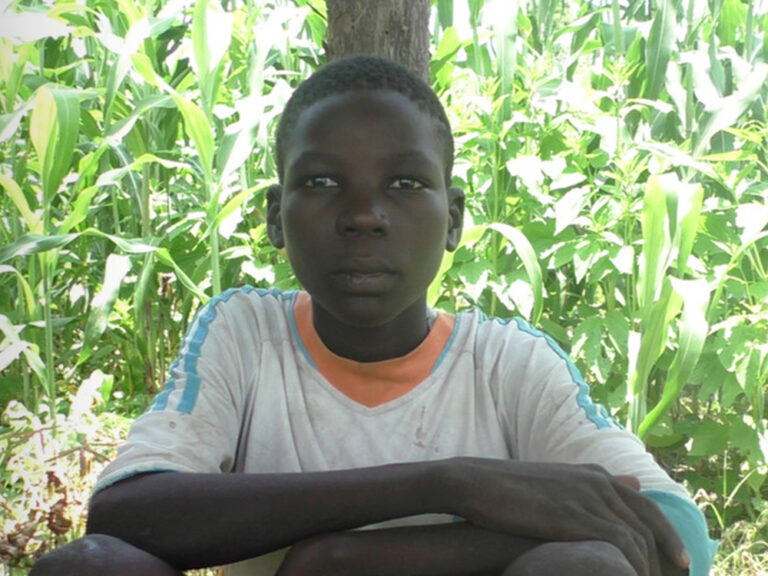 A young boy sat in front of a bush