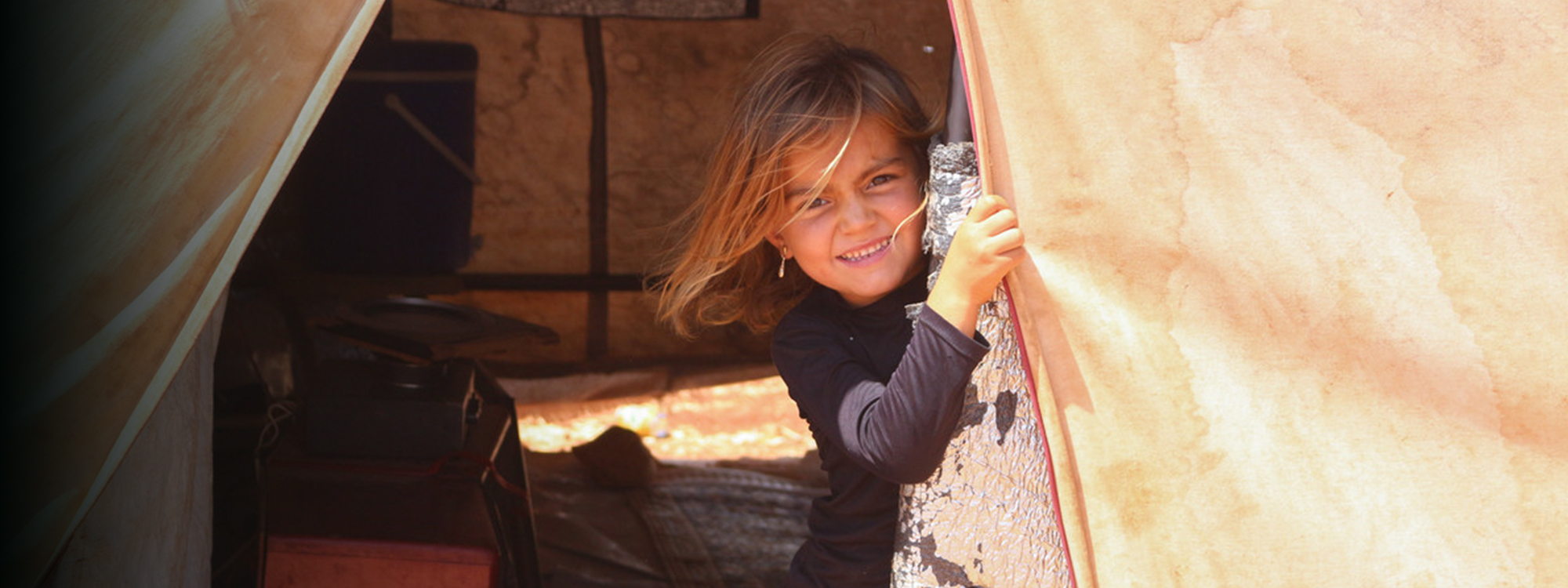A girl smiling through the door of a tent in Syria