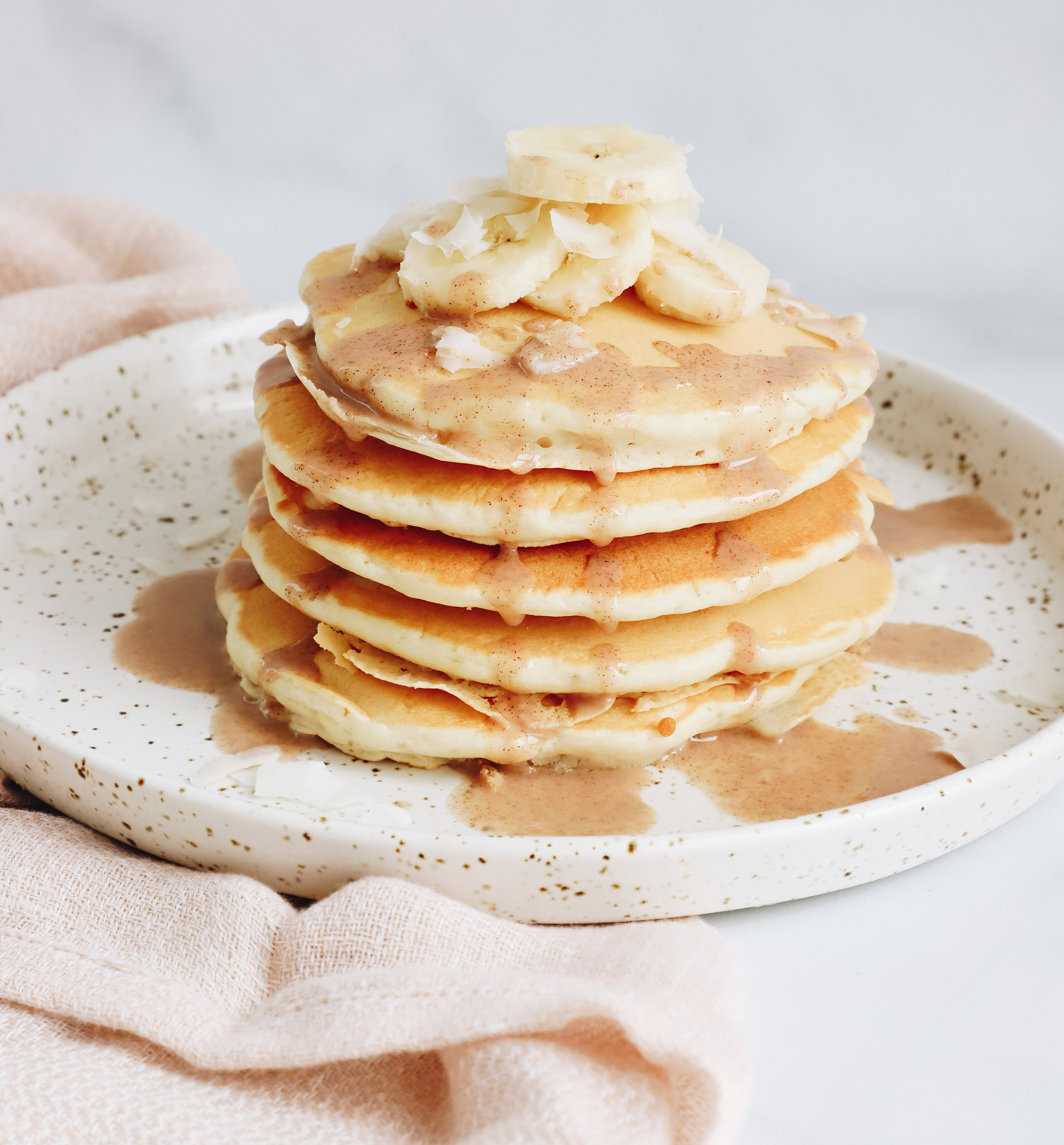 a stack of pancakes on a plate with pieces of banana and sauce on top