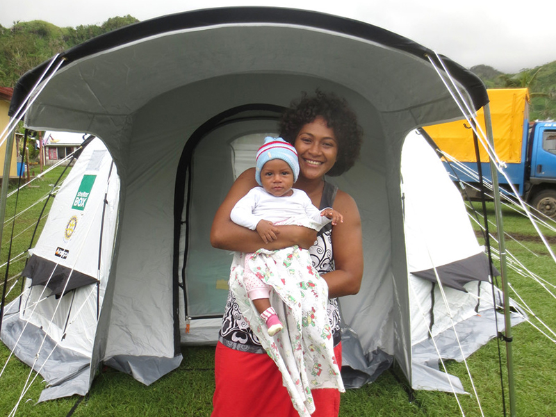 A woman smiling outside a tent holding her baby