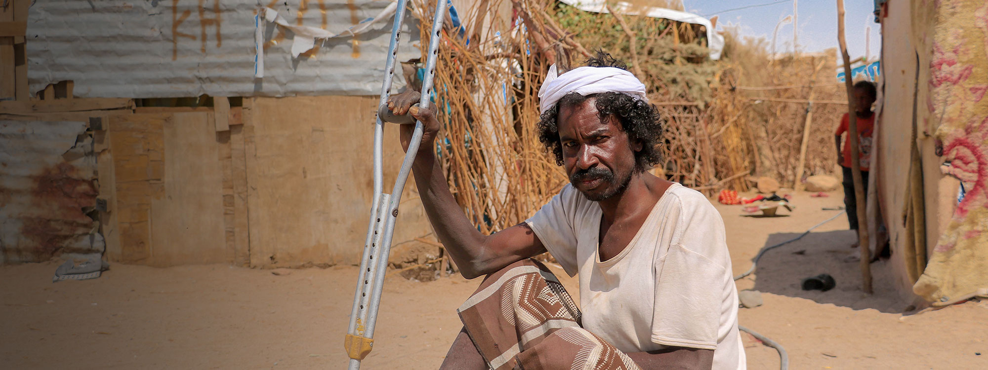 man sits in the sand with walking stick in yemen