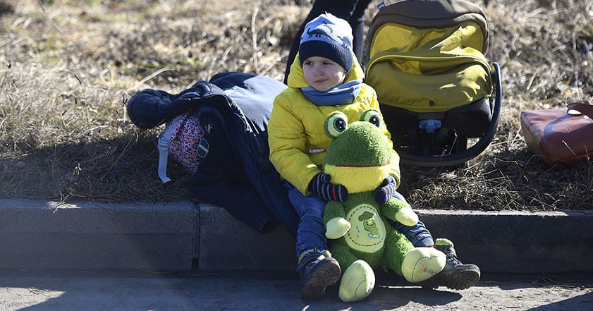Ukrainian boy sits at the roadside in yellow jacket