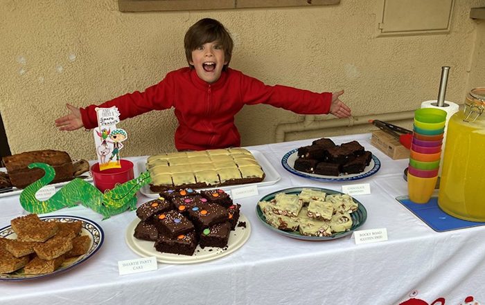 Boy sat next to table covered in cake for a bake sale