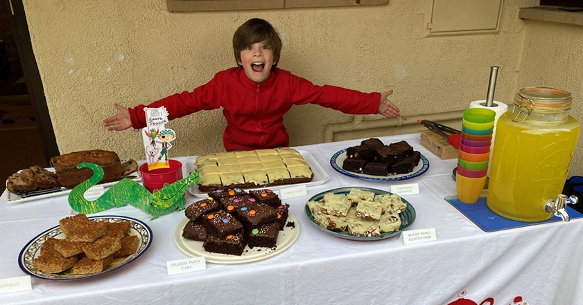 Boy sat next to table covered in cake for a bake sale