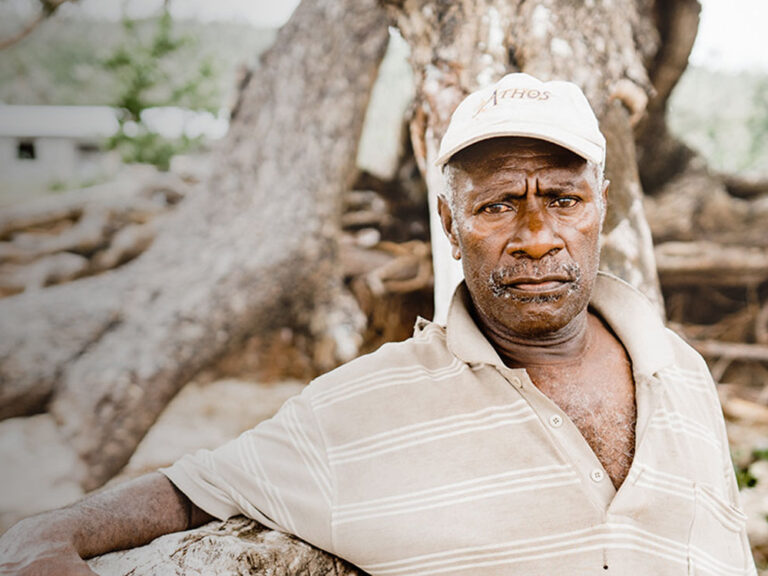 man in cap stands-at the foot of banyan tree in vanuatu