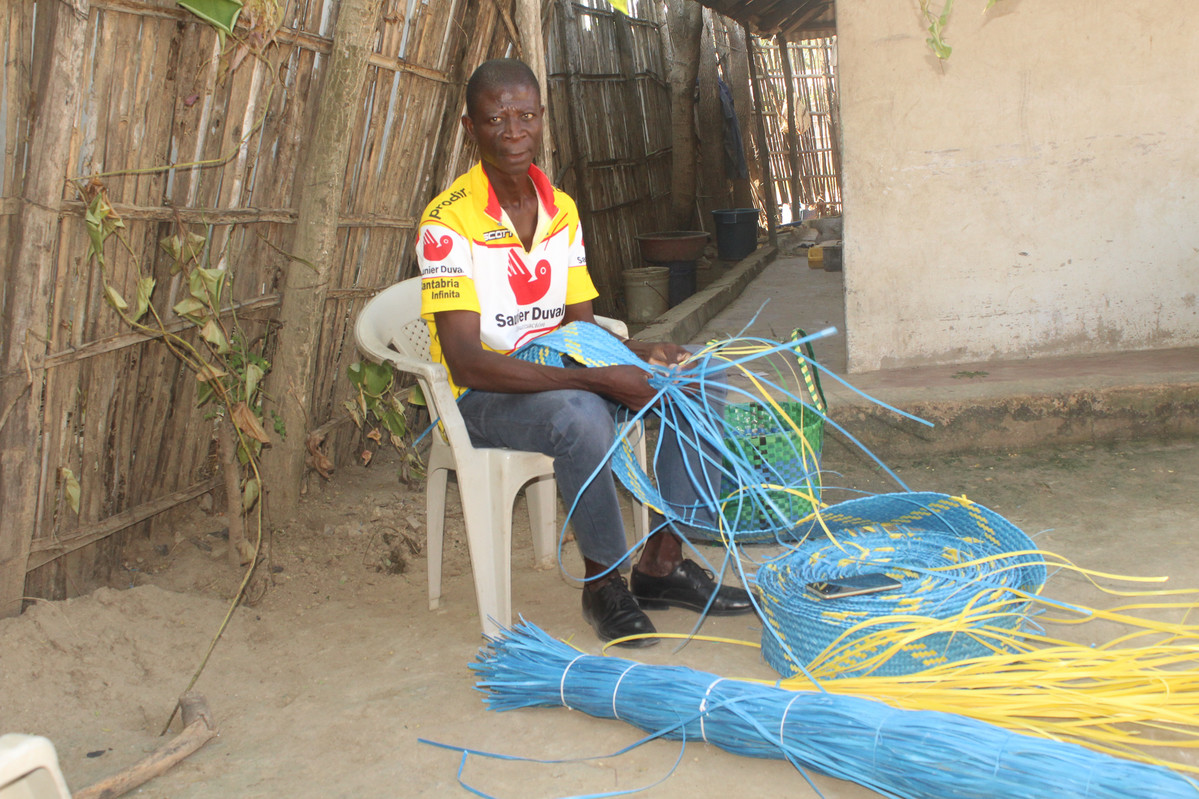 Man weaving a basket from strips of plastic waste