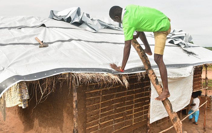 Man repairing roof in Mozambique with a tarpaulin