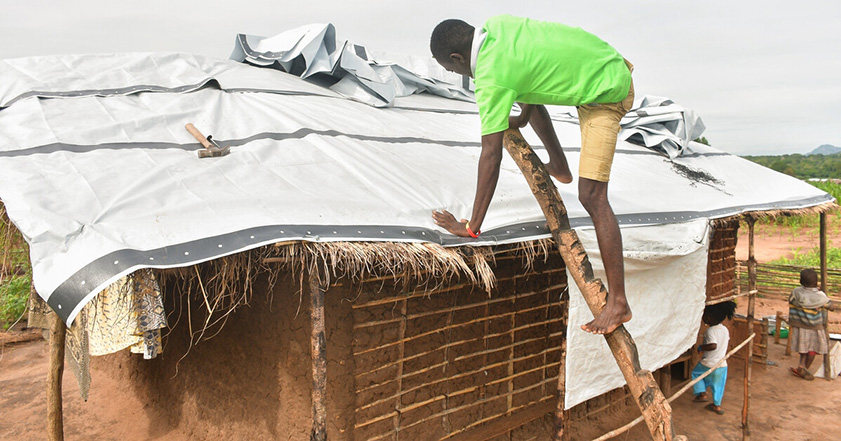Man repairing roof in Mozambique with a tarpaulin