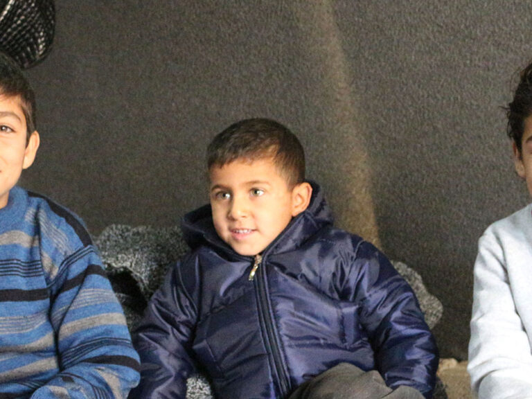 three young siblings from Syria sitting on mattresses smiling