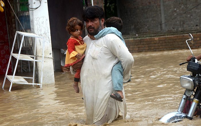 Man carrying two children through floodwater in Pakistan
