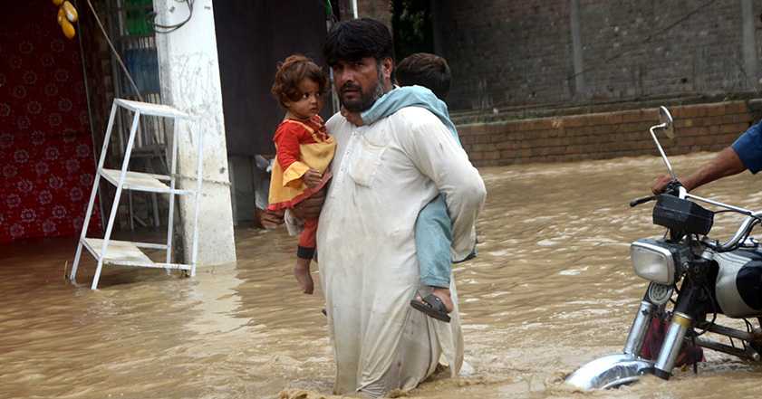 Man carrying two children through floodwater in Pakistan