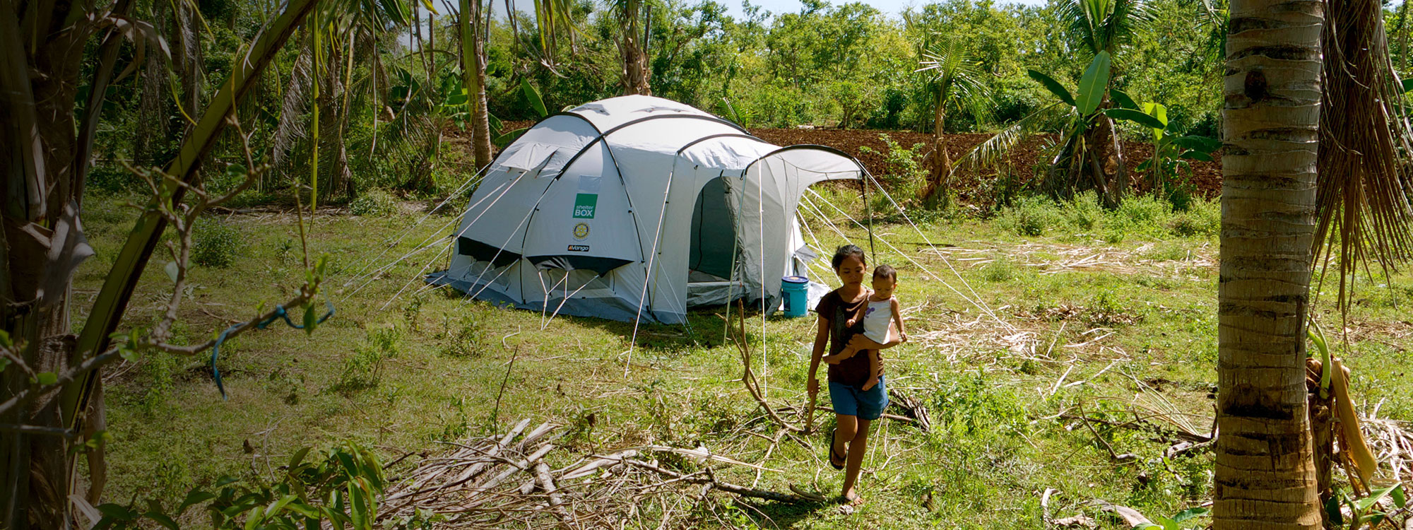 woman carrying baby in front of shelterbox tent in the philippines