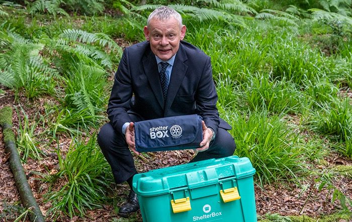 Martin Clunes wearing a suit next to a ShelterBox