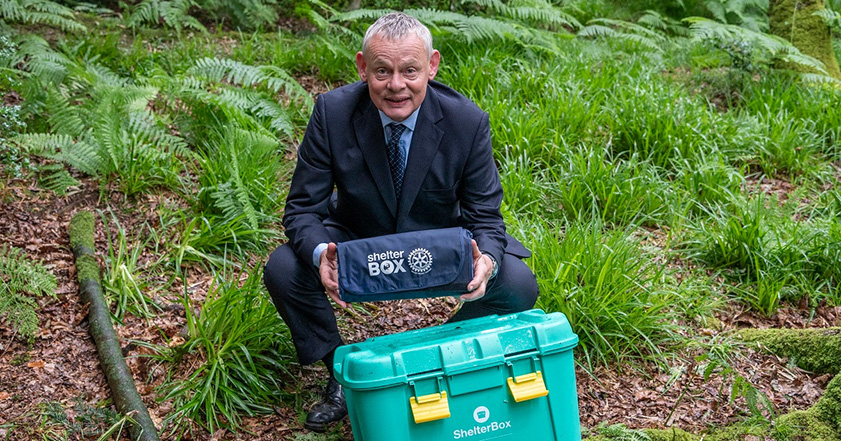 Martin Clunes wearing a suit next to a ShelterBox
