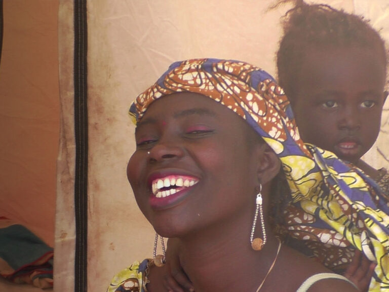 Cameroon - woman in headscarf smiling with child standing behind her