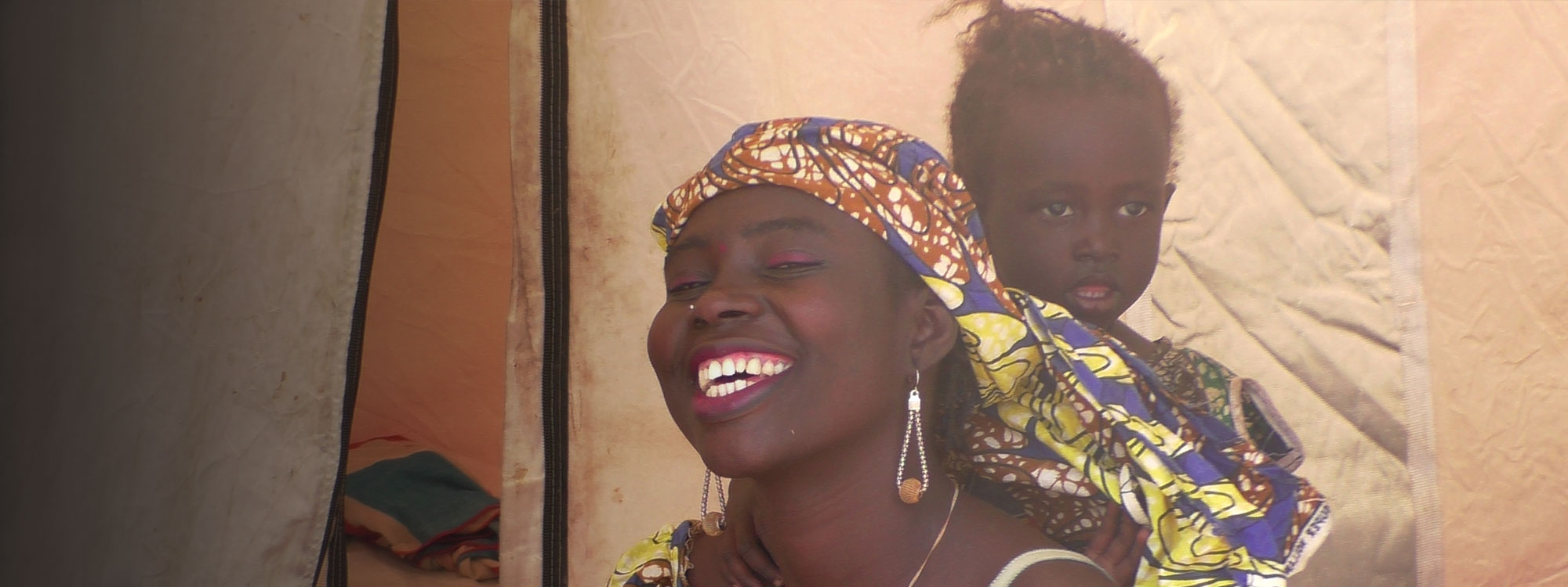 Cameroon - woman in headscarf smiling with child standing behind her