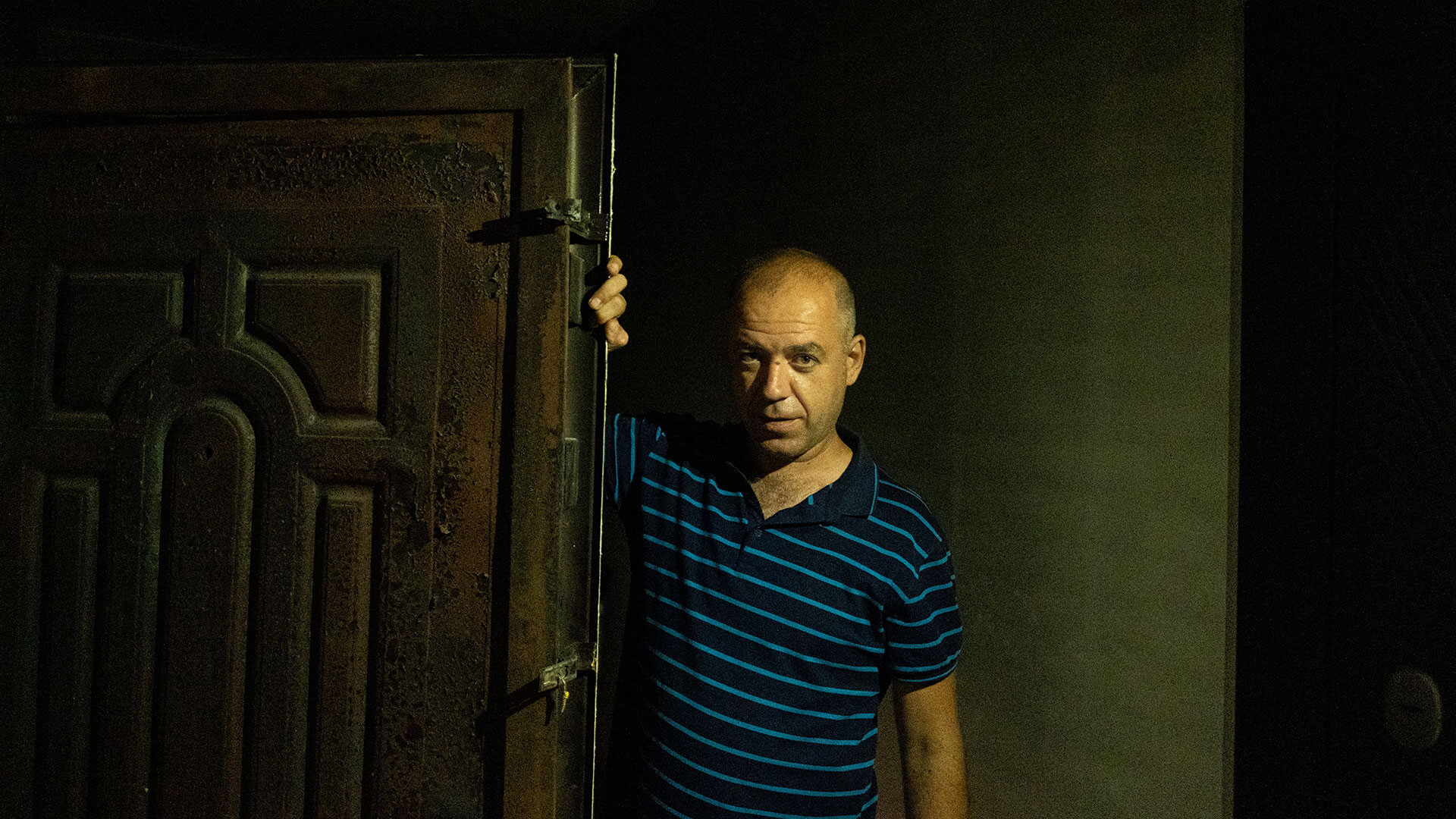Man stands in darkness leaning on the door of his damaged home in Ukraine