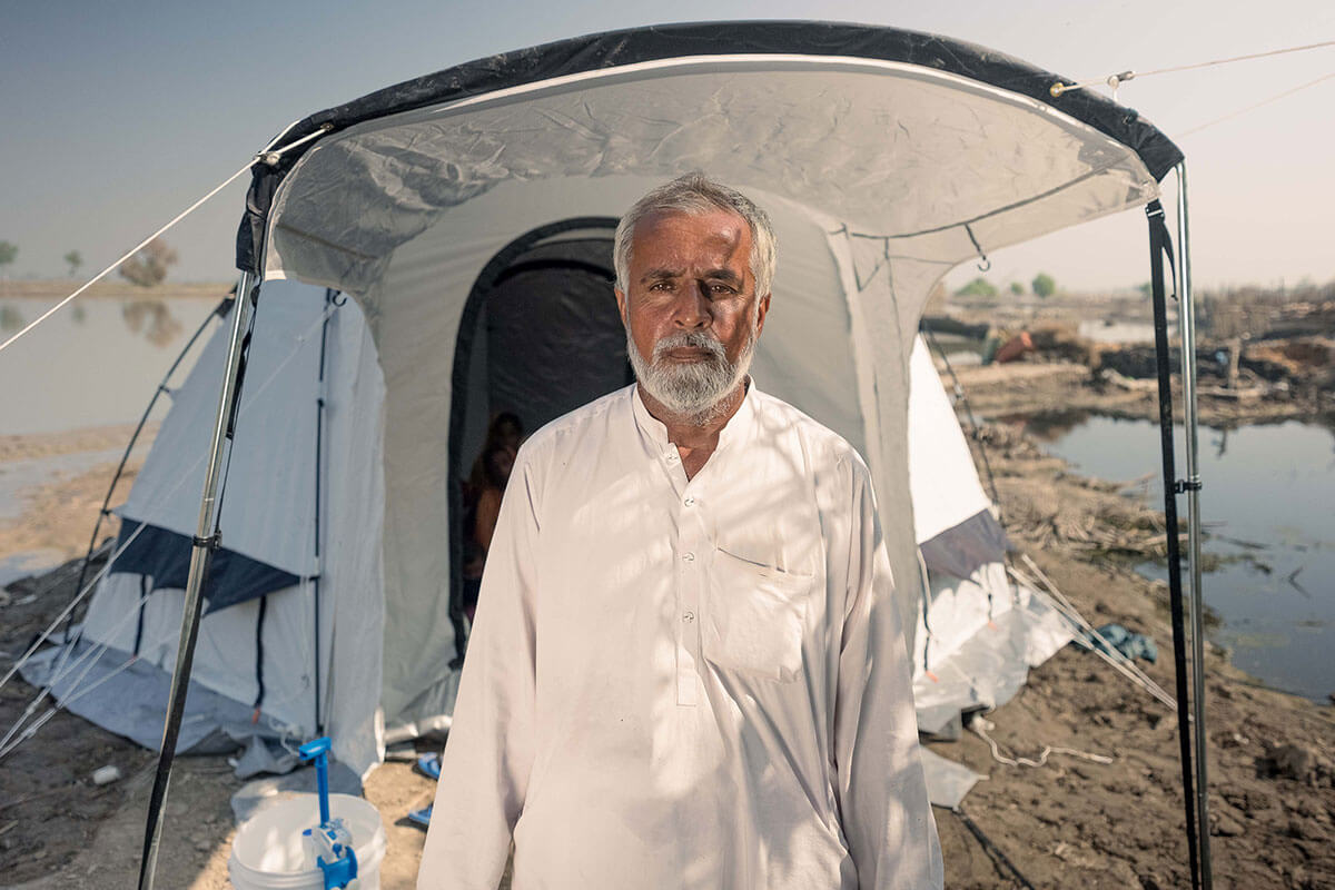 Man stands unsmiling outside emergency relief tent after flooding in Pakistan